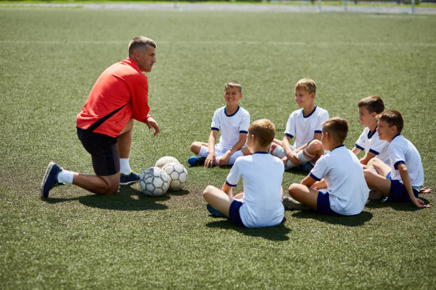 Entraîneur agenouillé face à des jeunes joueurs en cercle sur un terrain de soccer