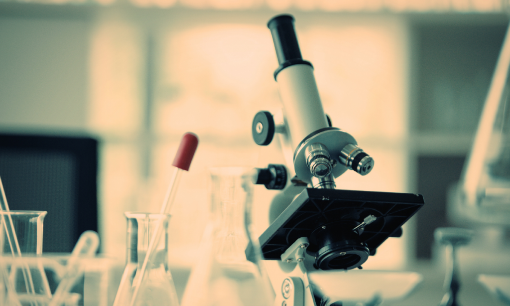 Microscope de laboratoire et verrerie scientifique en arrière-plan flou, évoquant la recherche et la formation en neurosciences à la Faculté de médecine